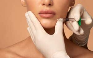 Woman receiving filler injections for chin contouring, with beautician holding syringe during non-surgical chin enhancement procedure
