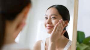 Woman touching her smooth facial skin while looking in the mirror, considering laser peels for beauty treatment